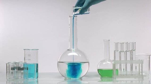 Pouring blue solution in flat bottomed flask with clean transparent swirling liquid, water quality control test, chemistry experiment.
