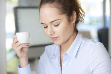 Starting working day with coffee. Close-up shot of a young businesswoman sitting at office and drinking coffee early morning.