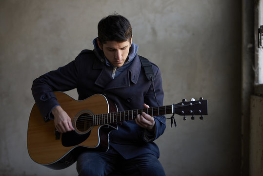 Close-up shot of a young musician playing his acoustic guitar. 