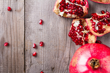 Broken and whole red ripe juicy pomegranates on rustic wooden unpainted table