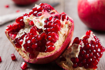 Whole and broken red ripe juicy pomegranates on rustic wooden unpainted table