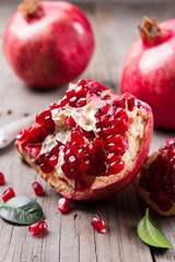 Whole and broken red ripe juicy pomegranates on rustic wooden unpainted table