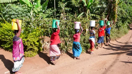 Fototapeten Frauen tragen Wasser vom Dorfbrunnen zu ihren Häusern in Tansania in Afrika © makasana photo