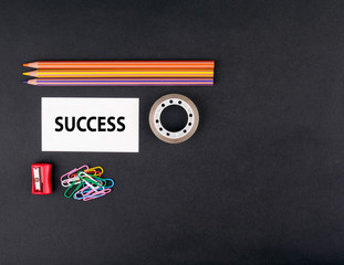 SUCCESS. Top view of a black ofice desk. Colored pencils, busine