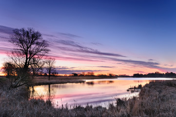 Dawn with pink clouds over a wild pond surrounded by trees in autumn morning