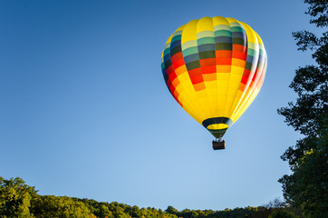 Naklejka premium Kolorowy balon na gorące powietrze unoszący się nad lasem o zachodzie słońca