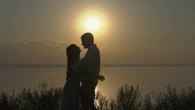 Happy young couple hugging and kissing near the sea on the sunset. Concept of love and relationships slow motion.