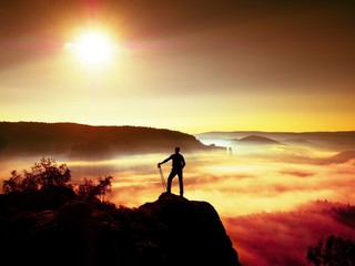 Tall backpacker with poles in hand. Sunny misty daybreak in rocks