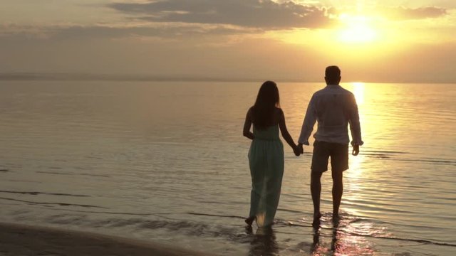 Young happy couple walking on the beach on the sunset. Concept of love and relationships slow motion.