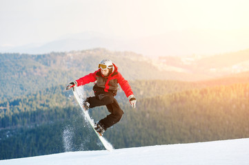 Man boarder jumping on his snowboard and taking his for the edge on top of a mountain against the...