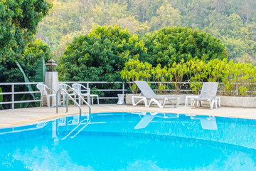 Blue swimming pool with chairs and sunbeds. They are used for relaxation and leisure activities.