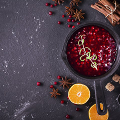 Fresh homemade cranberry sauce in a pan on dark wooden background with scattering of ripe berries.