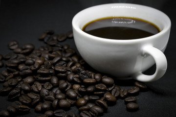 Closeup coffee beans and white ceramic coffee mug on the dark background.