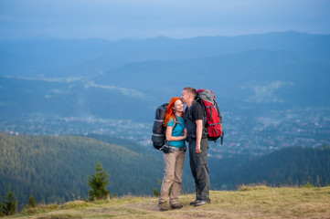 Obraz premium Tourists man and red-haired woman standing facing each other and smiling on the road in the mountain on the background of the landscaped mighty mountains