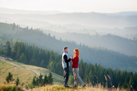 Happy guy and girl standing facing each other on a hill at the mountains in the morning. Lifestyle active vacations concept mountains and forests landscape on background