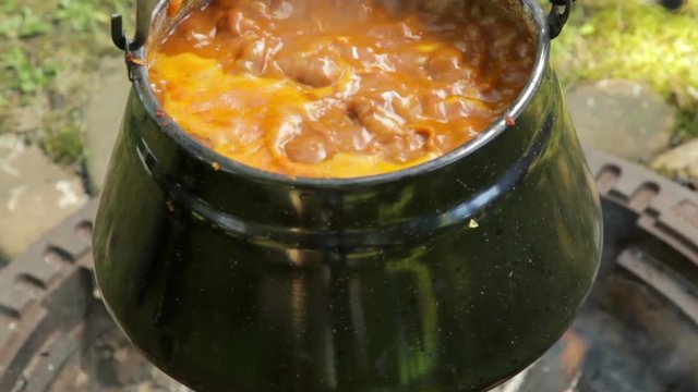 close-up of a boiling goulash soup in a vintage kettle hanging over a campfire