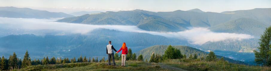 Fototapeta na wymiar Back view man holding hands red-haired woman standing on a hill,