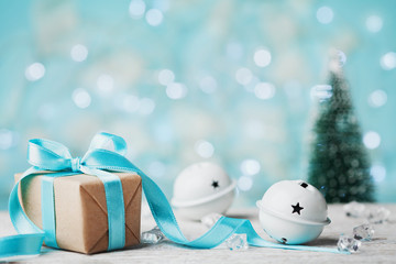 Christmas gift box, jingle bell and blurred fir tree against blue bokeh background. Holiday greeting card.