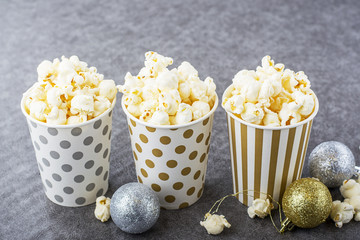 Salty fresh crusty homemade popcorn in silver paper cup in the fashion light background of white brick wall in a New Year's interior with Christmas balls. selective focus
