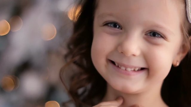 little girl three years old in a white dress smiling at the decorated Christmas tree in room