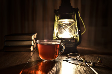 Naklejka na ściany i meble The light of kerosene lamp, cup of tea and books on the table