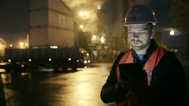 Engineer in hardhat with a tablet computer looks at truck on heavy industry factory