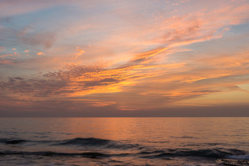 Sunset light reflected in bright orange colors on high clouds over the sea