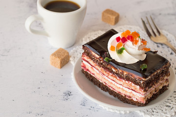 Chocolate cake and coffee .   Chocolate cake with cream on a plate, coffee cup,a fork and two pieces of sugar on a light table.