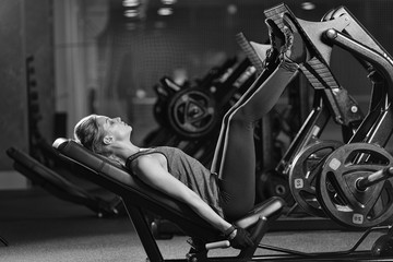 Sportive woman using weights press machine for legs at the gym. Pretty brunette exercising in a...