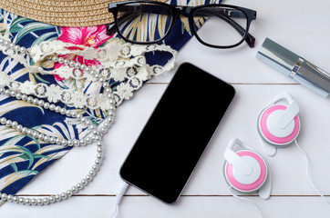 Workspace with smartphone, eyeglasses, sun hat, cosmetics and earphones on wooden background. Top view of female accessories with copy space.