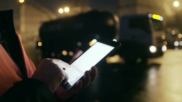 Engineer works on tablet computer and watches at big trucks at heavy industry factory