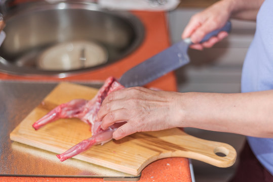 Senior woman hands cutting raw rabbit meat on a wodden table. Shallow dof, selective focus on woman hand.