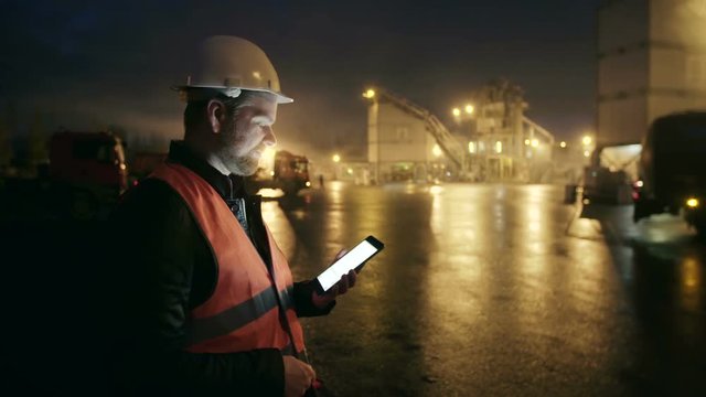 Engineer with tablet computer looks at camera at heavy industry factory