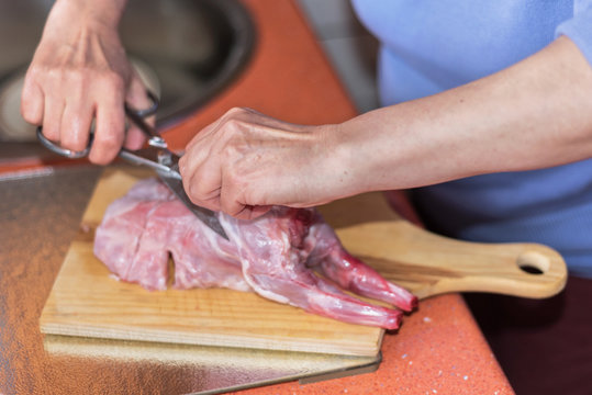 Senior woman hands cutting raw rabbit meat on a wodden table. Sh