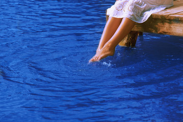 Fototapeta premium Relaxation. Young woman wets feet in water. (Sea, ocean, travel)
