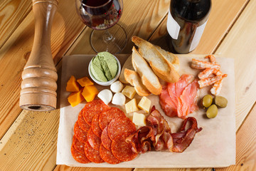 antipasti platter on wooden surface. bottle and glass of wine. different snacks