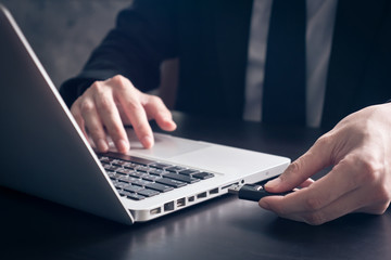 Close up of Businessman using flash drive connect to laptop on the desk. - obrazy, fototapety, plakaty