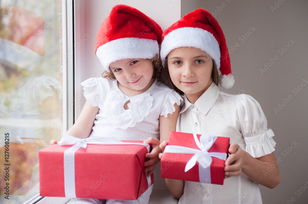 Wall mural two little sisters in Santa hats holding boxes with gifts