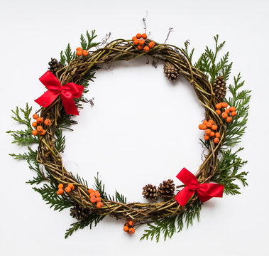 Festive wreath of vines with decorative bows, thuja branches, rowanberries and cones. Flat lay, top view