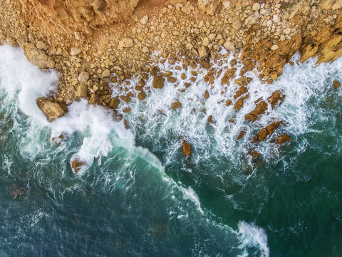 Aerial. Waves swim to the rocky shore.