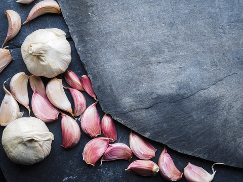 Red garlic cloves on dark slate backdrop