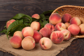 peaches in a wicker basket with leaves on wooden table