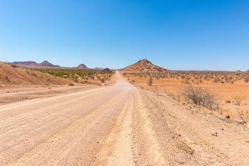 Gravel 4x4 road crossing the colorful desert at Twyfelfontein, in the majestic Damaraland Brandberg, scenic travel destination in Namibia, Africa.