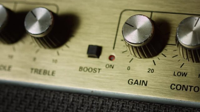 Close up of press boost button and turn up gain level on panel of guitar amplifier
