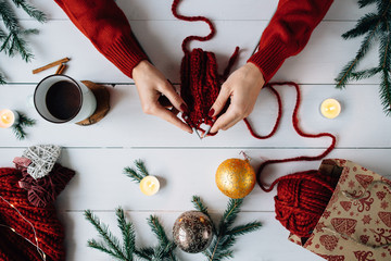 The woman knits Christmas things on white wooden background. Christmas composition.