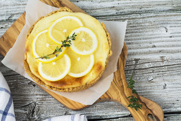 Fresh homemade cream cheese sweet cake for breakfast with slices of lemon and thyme on olive board  a simple light wooden background. selective Focus