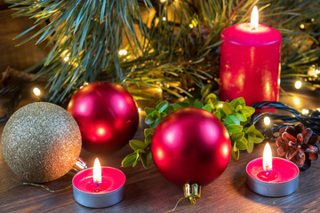 Light christmas candles and fir tree branch with lights decor and balls  on dark wooden background in vintage style. Coloring and processing photo