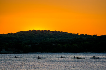 Gruppe Ruderer am Wasser bei Sonnenuntergang