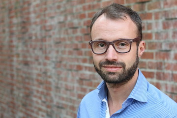 Mature man with glasses smiling isolated on brick wall background with space for copy