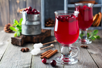 Fresh cranberry juice with cinnamon and anise in glass jars on the old wooden background. Selective focus.